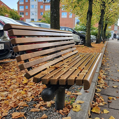 A wooden park bench with autumn leaves all around on the ground.